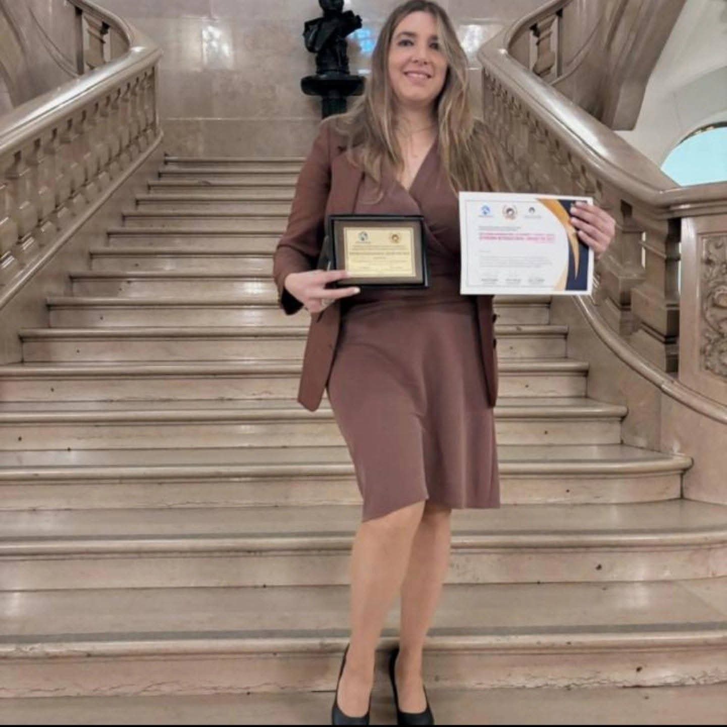 Laura Baston con diplomas y reconocimientos TRANSACADEMIA Honoris Causa